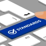 Standards Button With Check Mark On Laptop Keyboard With Fingers - Vector Illustration